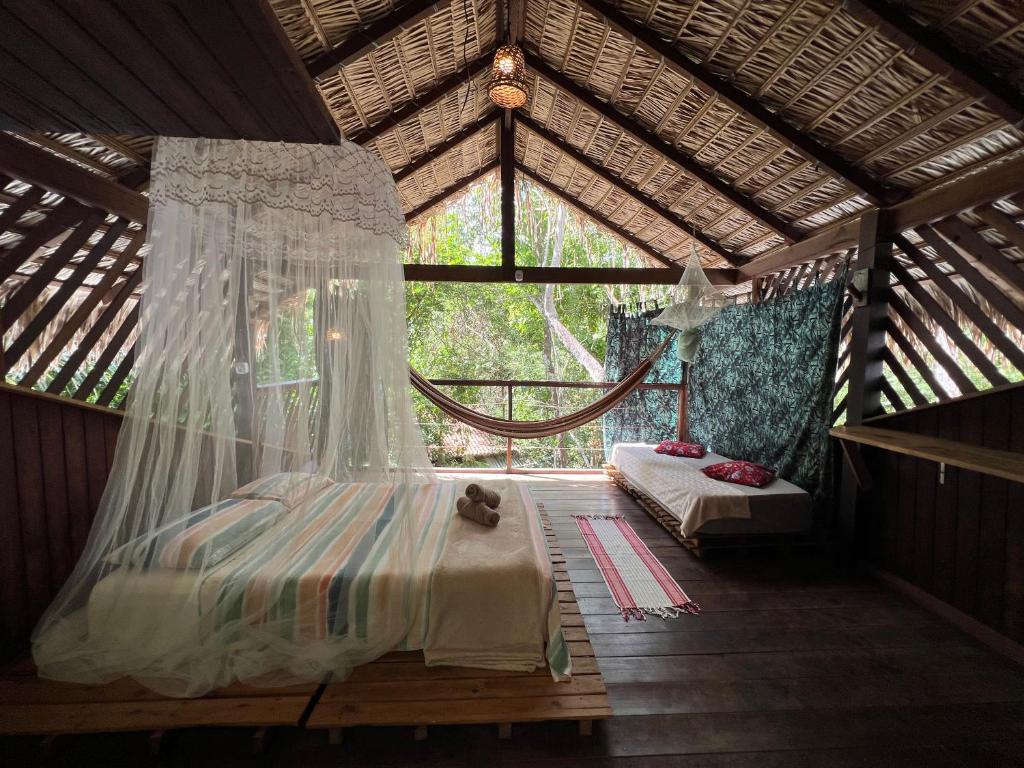 Cabana de madeira ao ar livre com uma cama sob um mosquiteiro, uma rede e um sofá-cama, cercada por árvores, da Vila Amz.