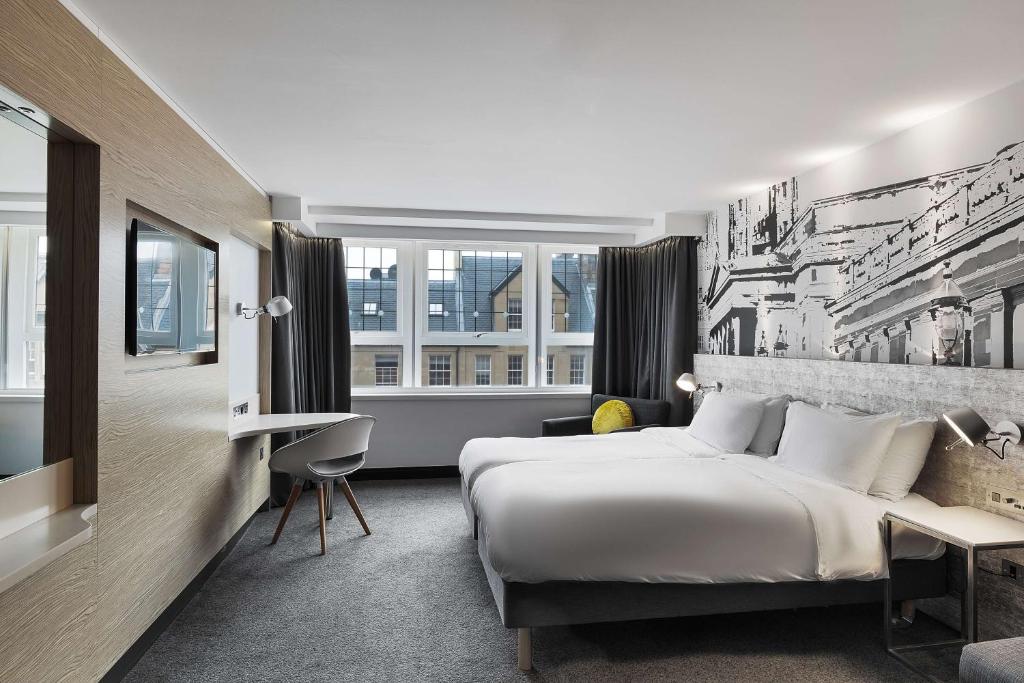 Quarto de hotel moderno no Radisson Blu Hotel com uma cama de casal, escrivaninha, TV, janelas grandes e um mural em preto e branco na parede. Ilustra o post de onde ficar em Edimburgo.