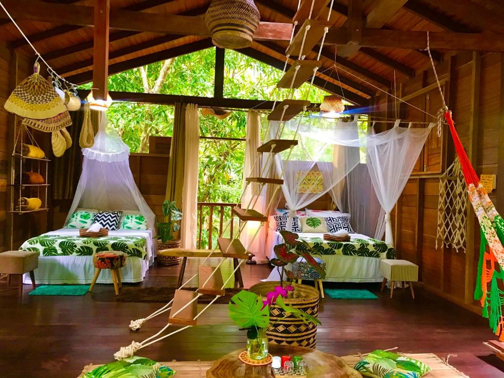 Interior de uma cabana de madeira com duas camas, mosquiteiros, uma rede, decoração suspensa e escadas que levam a um loft, da Casa da árvore. Representa hotéis em Alter do Chão.