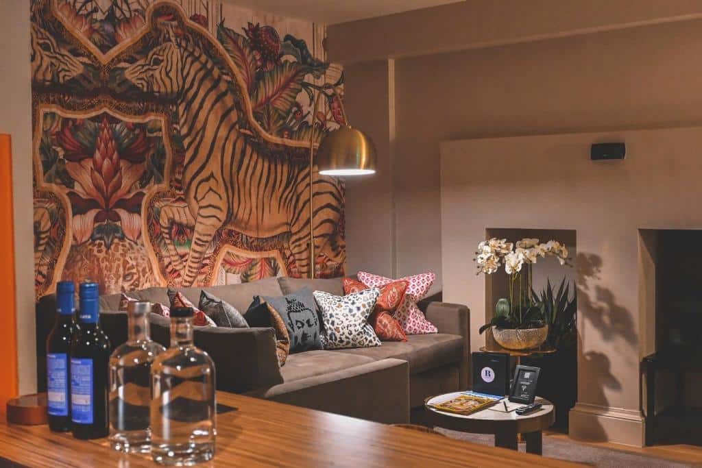 Uma sala de estar no The Rutland Hotel & Apartments com sofá, arte de parede com tema de animais e plantas, almofadas, garrafas, copos e vasos de plantas.