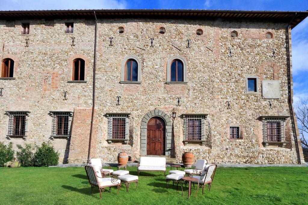 Edifício de pedra do Castello di Bibbione com janelas e porta em arco, área de estar externa com cadeiras e sofás em um gramado na frente. Imagem para ilustrar post sobre hotéis românticos na Toscana.