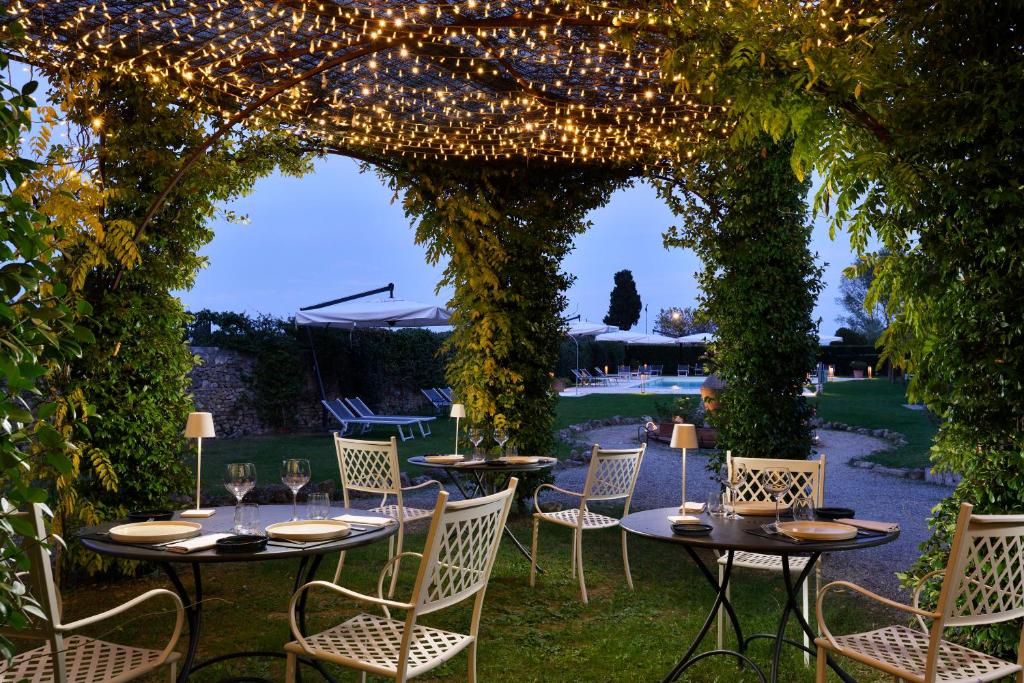 Área de jantar da Villa Sabolini ao ar livre com cadeiras e mesas brancas sob um dossel de luzes de corda, com vista para o jardim e a piscina. Imagem para ilustrar post sobre hotéis românticos na Toscana.