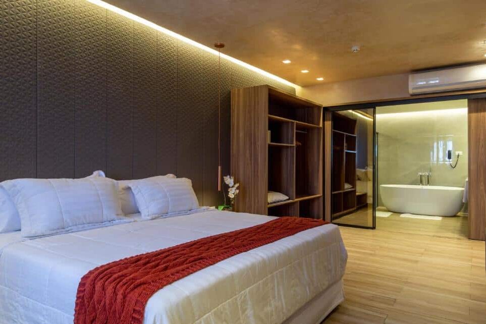 No Blue Tree Towers Rio Poty, um quarto com uma cama grande, cama vermelha, guarda-roupa de madeira e um banheiro aberto com uma banheira ao fundo. A foto faz parte do post de onde ficar em Teresina.