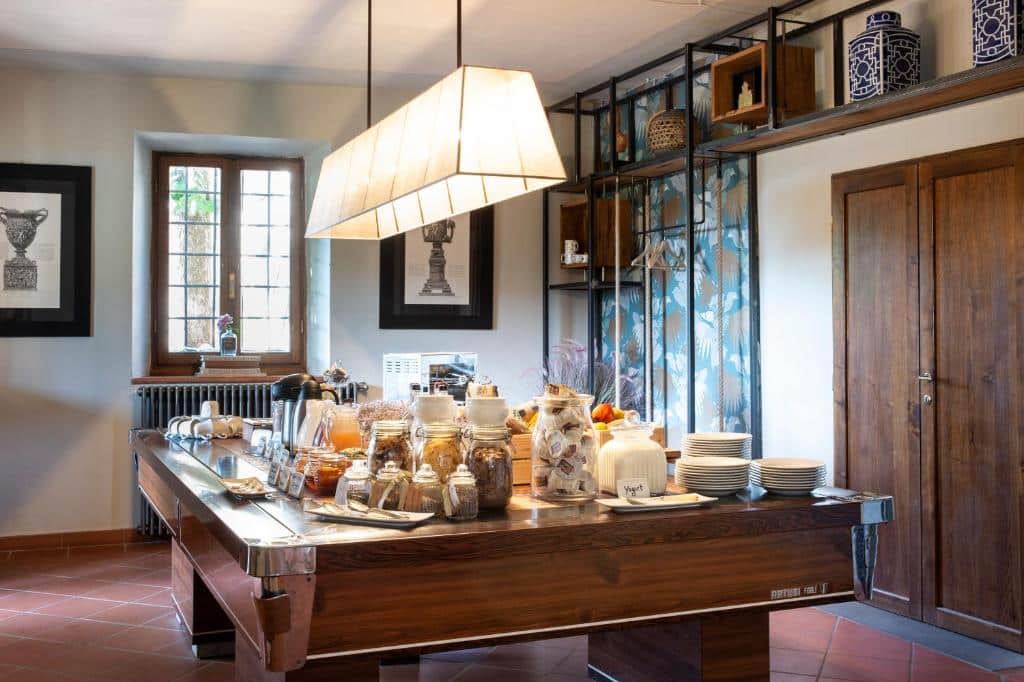 Um bufê do Borgo I Vicelli Adults com potes, pratos e itens de café da manhã em uma mesa de madeira em uma sala bem iluminada com decoração e arte emoldurada. Imagem para ilustrar post sobre hotéis românticos na Toscana.