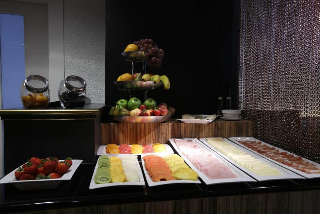 Um bufê de café da manhã do Capitol Boutique Hotel com frutas fatiadas, queijos, carnes, frutas inteiras e potes de geleia em um balcão de madeira.