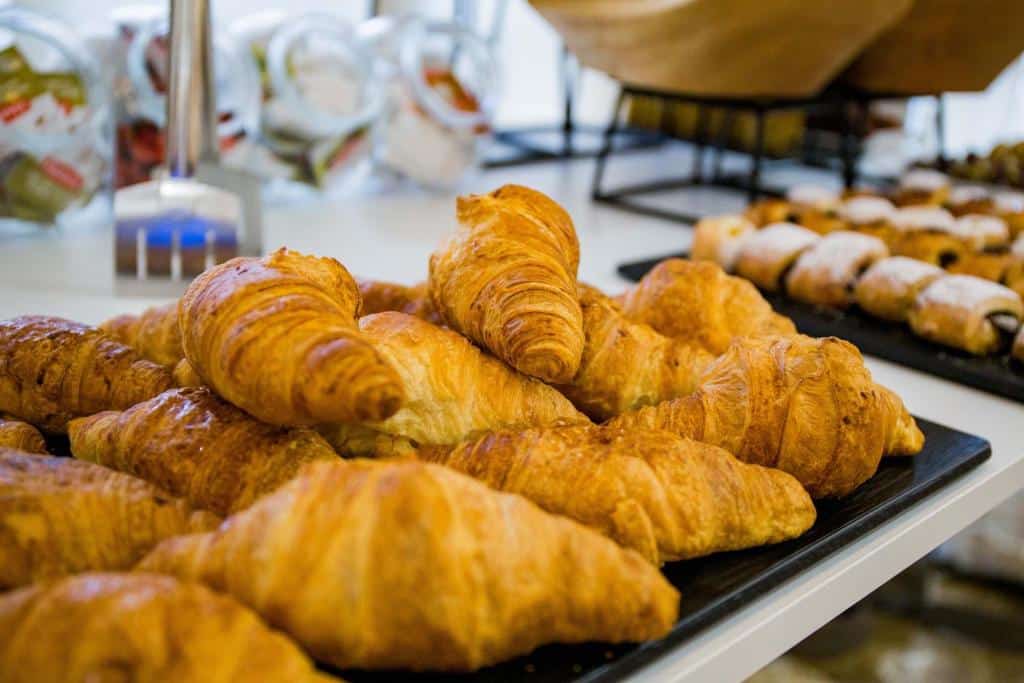 Uma bandeja de croissants em um balcão, com doces e potes de vidro ao fundo do Hotel Gelmírez. Imagem para ilustrar post sobre hotéis em Santiago de Compostela.