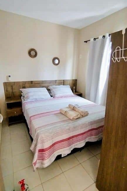 Chalet no paraíso. Uma cama bem arrumada com roupa de cama listrada, duas toalhas em cima e duas decorações de parede redondas em um quarto pequeno e arrumado.