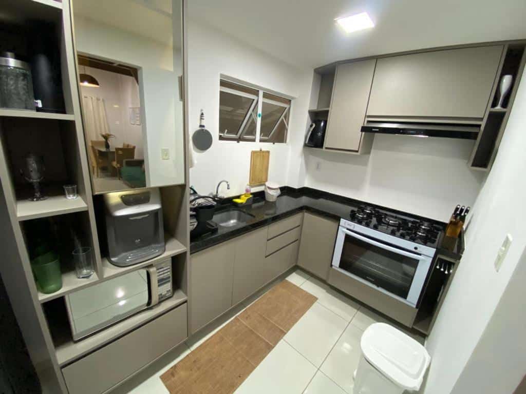 Cozinha moderna no Condomínio Village 4 Carneiros casa 40 com armários cinza, bancadas pretas, fogão, forno, micro-ondas, pia e vários eletrodomésticos e utensílios.