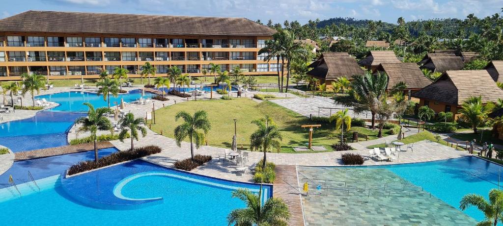 Eco Resort Praia dos Carneiros com piscinas externas, palmeiras, espreguiçadeiras e um edifício de hotel de vários andares ao lado de vilas em estilo tropical.