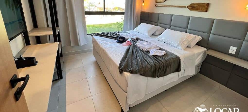 Quarto do Eco Resort Praia dos Carneiros com uma cama de casal, pás montadas na parede, TV, guarda-roupa aberto e janela grande com cortinas. Essa é uma das indicações de onde ficar na Praia dos Carneiros.