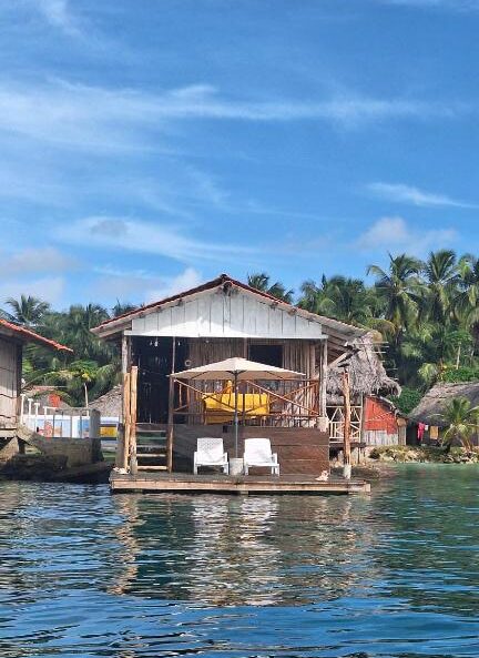 Fachada da Cabañas Narasgandup, uma cabana de madeira na água com espreguiçadeiras e um caiaque amarelo, cercada por palmeiras sob um céu azul. É uma das opções de onde ficar em San Blas.