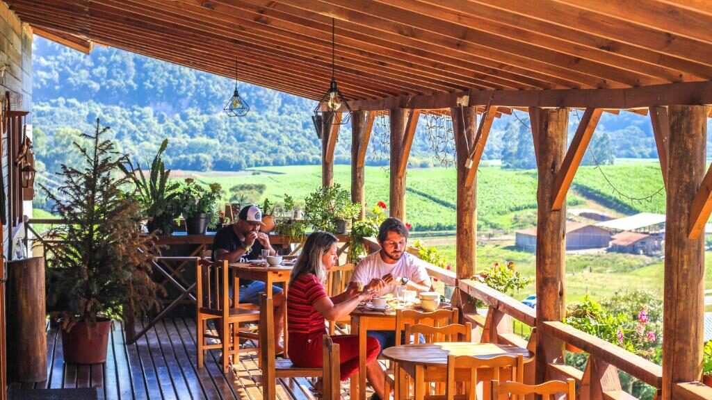 Casal apreciando paisagem campestre em varanda de madeira rústica da Hospedaria Kayser Haus com vista para campos verdes e montanhas. Essa é uma das dicas de onde ficar em Urubici.