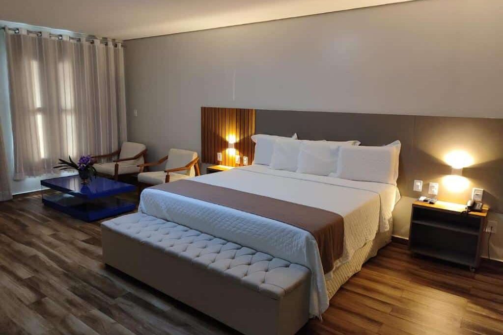 Hotel Reserva do Xingó, ilustra o post sobre pousadas em Piranhas. Quarto de hotel espaçoso com uma cama king size, duas cadeiras, um banco, mesas laterais com luminárias e piso de madeira.