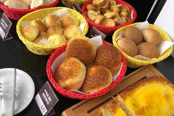 No Lis Hotel, pãezinhos variados e fatias de pão são exibidos em cestas e em uma tábua de corte em uma bancada preta.