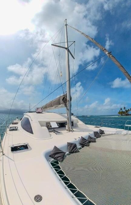 Vista do Enjoy Sailing Experience do convés de um veleiro catamarã branco no oceano sob um céu parcialmente nublado.