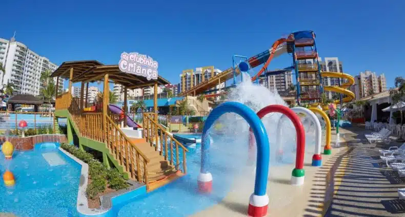 Parque aquático colorido do Prive Thermas Hotel com escorregadores, fontes e estruturas de recreação, cercado por prédios altos sob um céu azul claro. Imagem para ilustrar post sobre onde ficar em Caldas Novas.