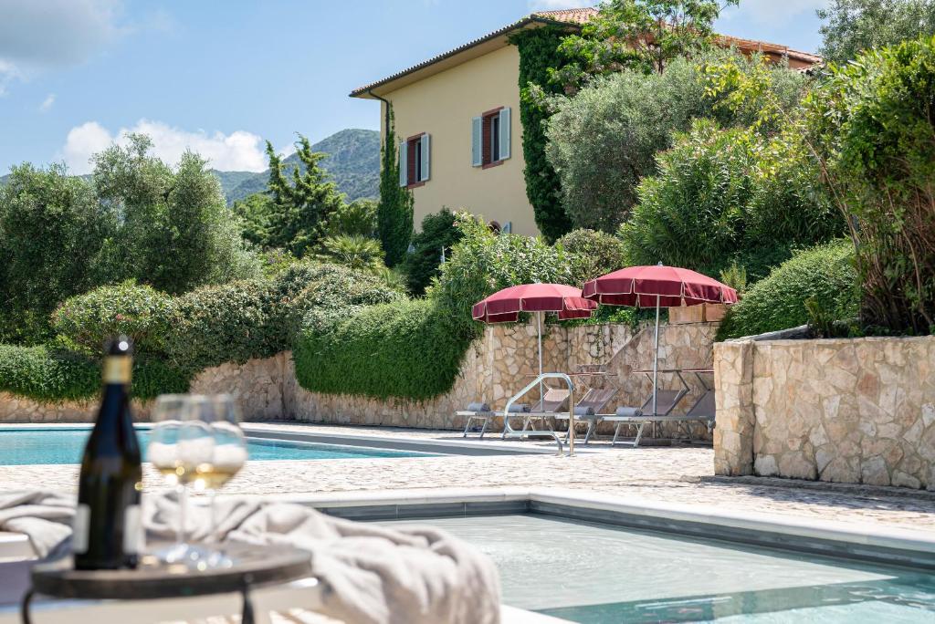 Uma piscina da La Muccheria com espreguiçadeiras e guarda-sóis vermelhos, com uma casa amarela e vegetação ao fundo.