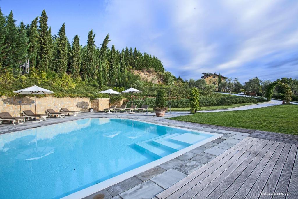 Piscina externa retangular do Relais Villa Belvedere com espreguiçadeiras, guarda-sóis, deck de pedra e área gramada, cercada por árvores e colinas. Imagem para ilustrar post sobre hotéis românticos na Toscana.