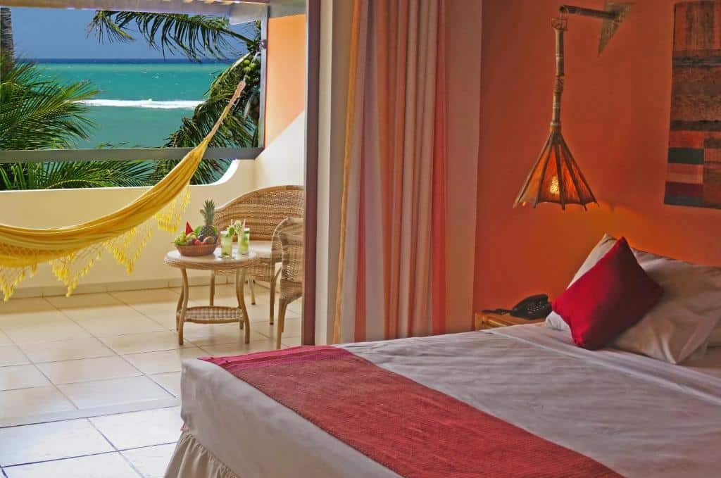 Quarto do Porto da Lua Boutique Hotel com uma cama, cadeiras de vime, uma rede amarela e vista para o oceano através de uma varanda aberta. Essa é uma das dicas de onde ficar na Praia do Forte.