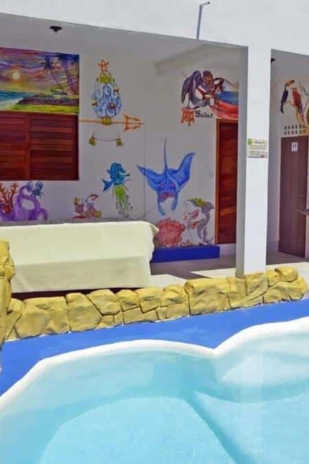 Pequena piscina externa com pedras, murais coloridos nas paredes e um grande peixe pintado perto da escada.