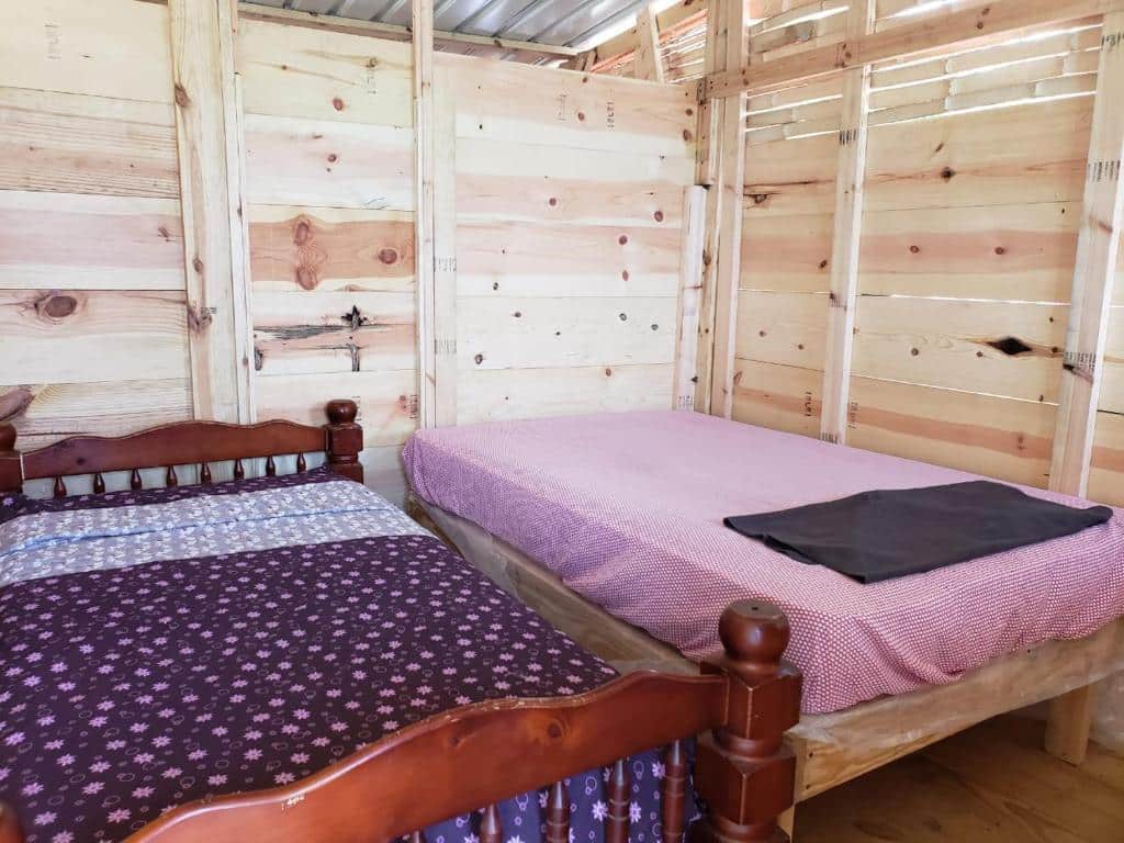 Duas camas de madeira com roupas de cama diferentes estão em um quarto do Private Room in San Blas Islands PLUS meals com paredes de tábuas de madeira inacabadas e piso de madeira. É uma das opções de onde ficar em San Blas.