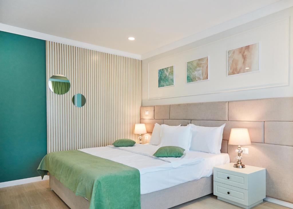 Um quarto moderno do Hotel Azaleea Mamaia Nord com uma cama de casal, cobertor verde, duas mesas de cabeceira com luminárias e três obras de arte emolduradas acima da cama.