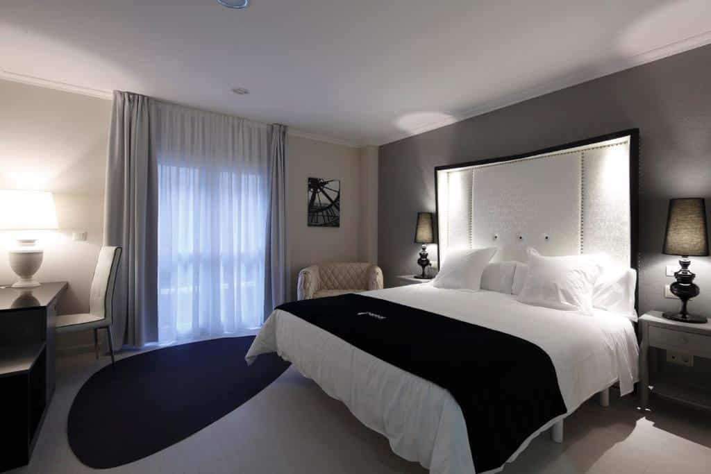 Um quarto do Capitol Boutique Hotel com uma cama grande, duas luminárias de cabeceira, uma escrivaninha, uma cadeira e uma janela com cortinas transparentes.