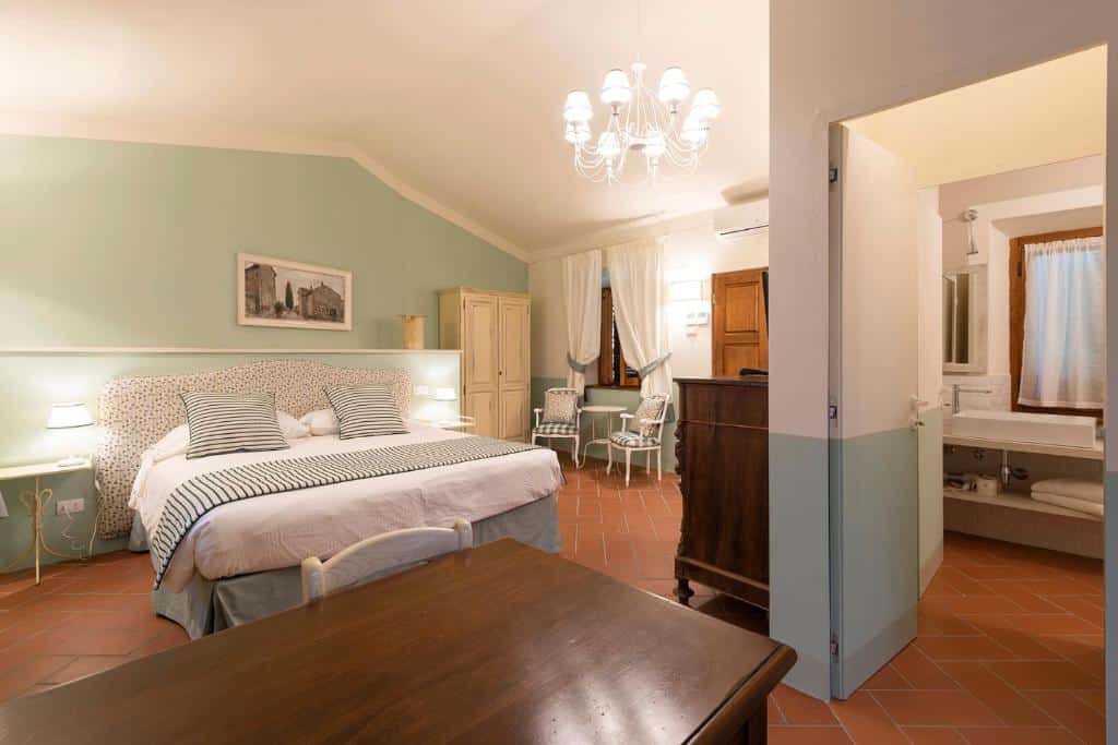 Um quarto do Il Palazzo bem arrumado com uma cama de casal, duas cadeiras, uma escrivaninha e uma porta aberta para um banheiro.