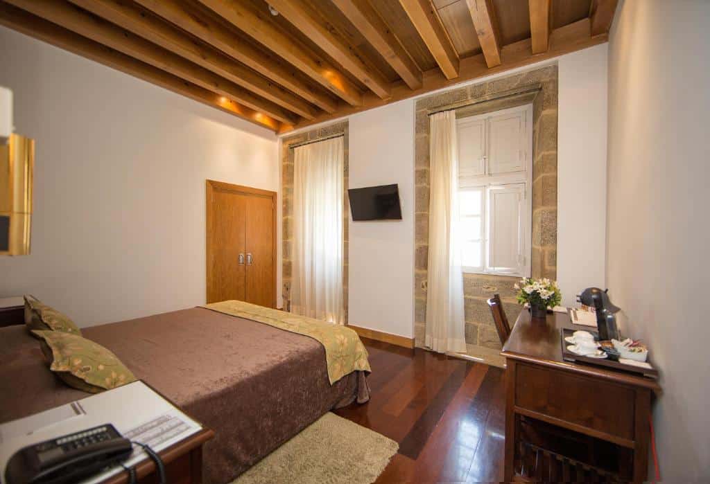 Quarto do San Francisco Hotel Monumento com uma cama de casal, teto de madeira, TV na parede, escrivaninha com amenidades e duas janelas grandes.