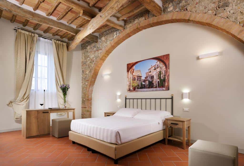 Um quarto da Villa Sabolini com uma cama de casal, móveis de madeira, paredes de pedra, vigas expostas e um grande arco de tijolos.