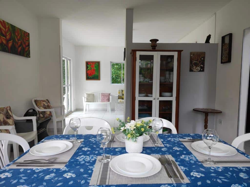 Uma mesa de jantar para quatro pessoas no Sitio Recanto Feliz com pratos e copos brancos em uma toalha de mesa azul, em uma sala moderna e bem iluminada.