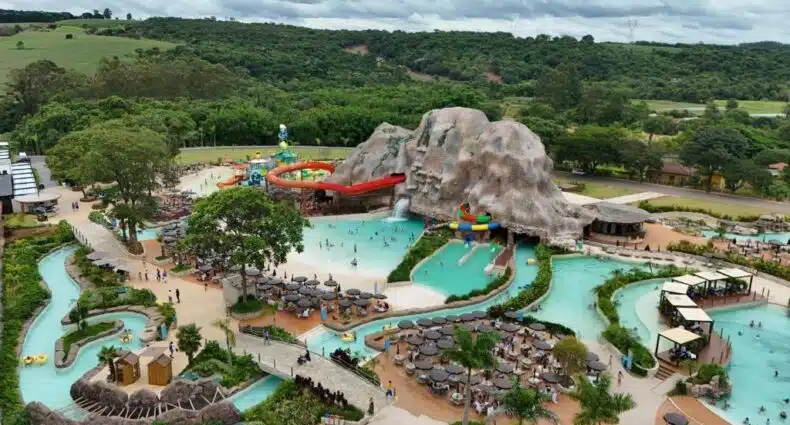 Vista aérea de um parque aquático com piscinas, toboáguas, um rio lento e uma grande estrutura de rocha artificial, no Tauá Hotel & Convention Atibaia, para representar onde ficar em Atibaia.