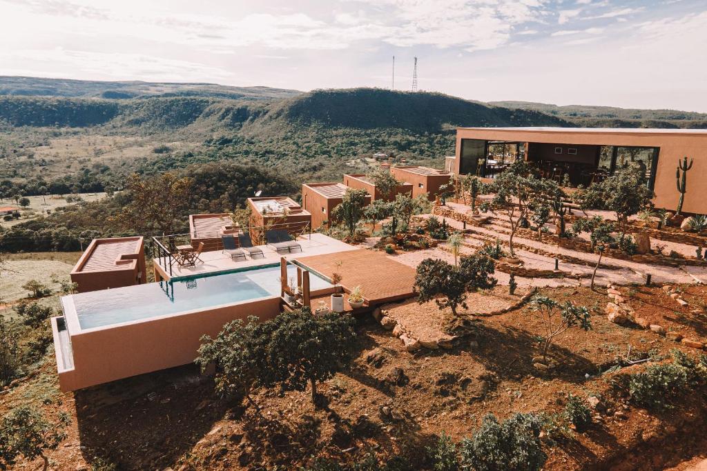 Pousada Vila Toá na encosta de uma colina em Alto Paraíso do Goiás, com piscina de borda infinita, edifícios modernos e colinas verdes ao redor, sob um céu parcialmente nublado.