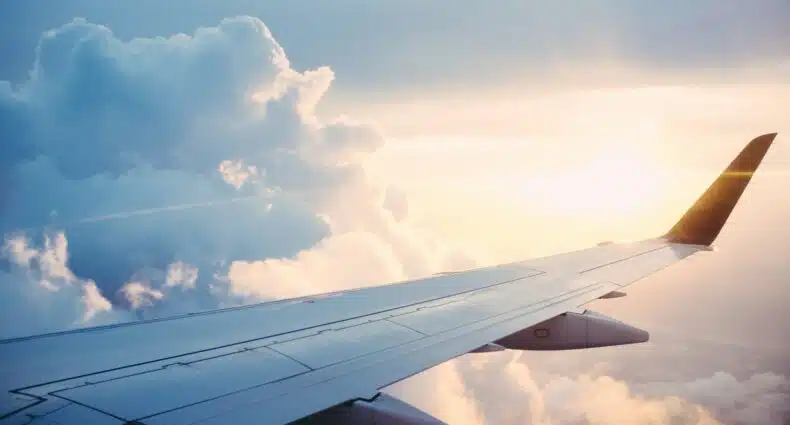 Avião em voo durante pôr do sol com céu azul e nuvens macias para ilustrar o post sobre o programa de fidelidade Genius Booking