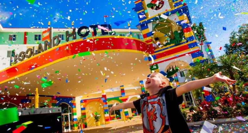 Criança animada brincando no Legoland Hotel, na Flórida, um parque temático e colorido da Disney, com confete voando no ar. Representa resorts para crianças