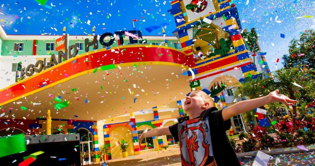 Criança animada brincando no Legoland Hotel, na Flórida, um parque temático e colorido da Disney, com confete voando no ar. Representa resorts, como um dos lugares para viajar com crianças
