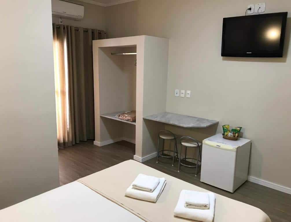 Quarto do Hotel Portal das Águas com cama, televisão de tela plana, armário embutido e frigobar.