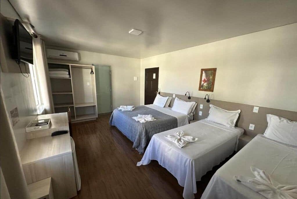 Quarto da Pousada Casarão Schmidt com camas de casal e armário embutido, decorado com quadro de arte e paredes claras, criando um ambiente confortável e acolhedor. Essa é uma das indicações de onde ficar em Pomerode.