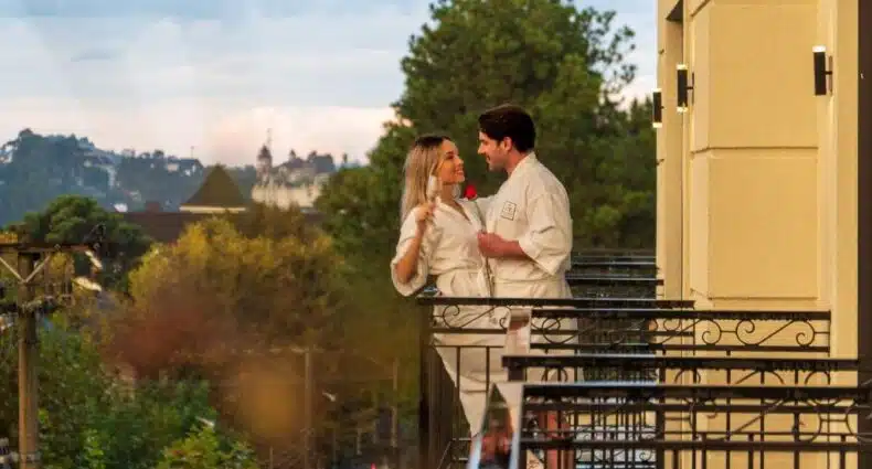 Casal apaixonado em roupão branco olhando um para o outro na varanda d\ Pousada D'Biagy Premium com vista para o Capivari e natureza. Represente um dos hotéis em Campos do Jordão