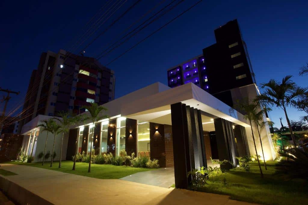 Uchôa Teresina Hotel iluminado à noite em área verde com palmeiras, no bairro de Jóquei, ambiente sofisticado.