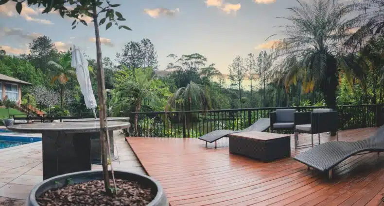 Deck de madeira do Village du Lac Hotel com móveis de vime pretos, piscina, vegetação tropical e céu nublado ao pôr do sol numa das dicas de onde ficar em Pomerode.