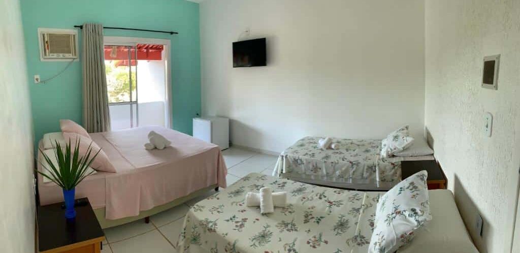 Quarto acolhedor da Vivenda Xawã com decoração floral em tons neutros, cama de casal com lençol estampado e poltrona, janela iluminando o ambiente. Essa é uma das dicas de onde ficar em Corumbau.