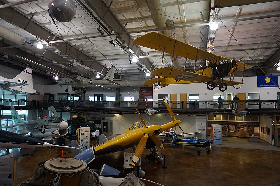 Hangar de exibição do Frontiers of Flight Museum com aeronaves históricas, incluindo um biplano amarelo em primeiro plano.