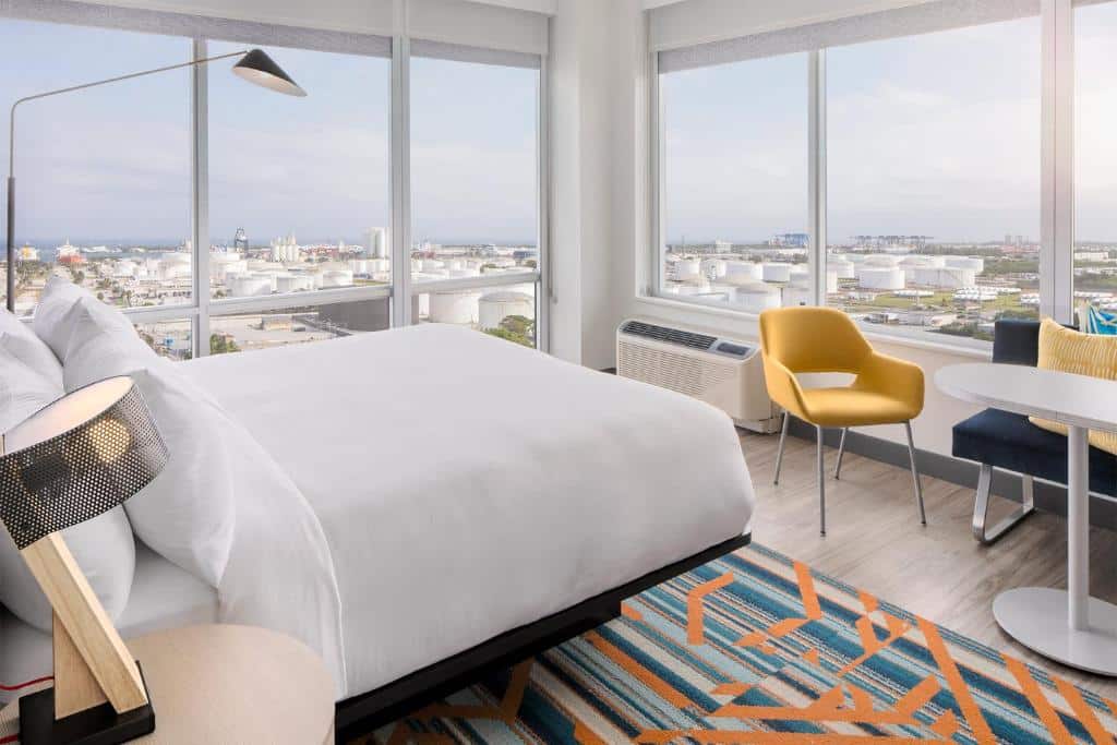 Quarto aconchegante do Aloft Fort Lauderdale com vista panorâmica da cidade, cama confortável e móveis modernos em tons claros e amarelo.