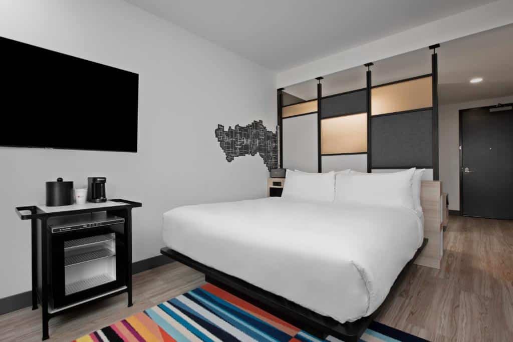 Quarto do Aloft Kansas City Country Club Plaza com parede decorada com mapa urbano preto e branco, TV de tela plana, frigobar e cama de casal com lençóis brancos.