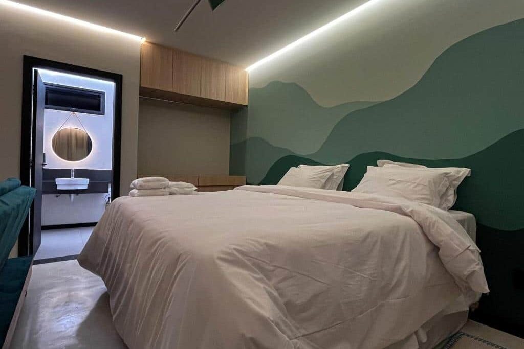 Quarto do Apart-hotel Theotókos Flats moderno com cama de casal, paredes verdes em degradê e armário de madeira.