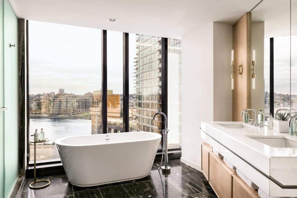 Banheiro de luxo do JW Marriott Parq Vancouver com vista panorâmica da cidade, com banheira freestanding e armários de madeira.