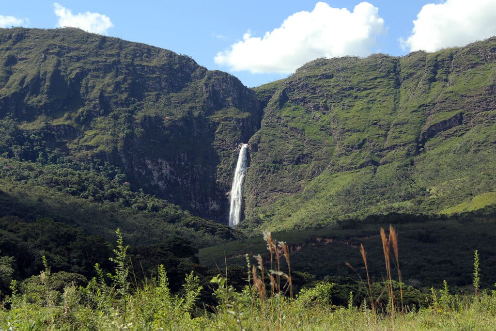 Cachoeira Casca D'Anta emoldurando belas montanhas verdes cobertas por nuvens brancas no céu azul, em paisagem natural majestosa.