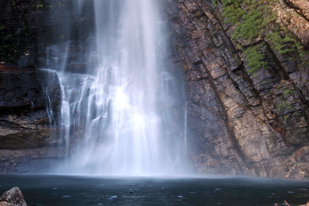 Cachoeira Casca D'Anta caindo por entre rochas escarpadas em densa floresta verde, criando poça de água cristalina abaixo.