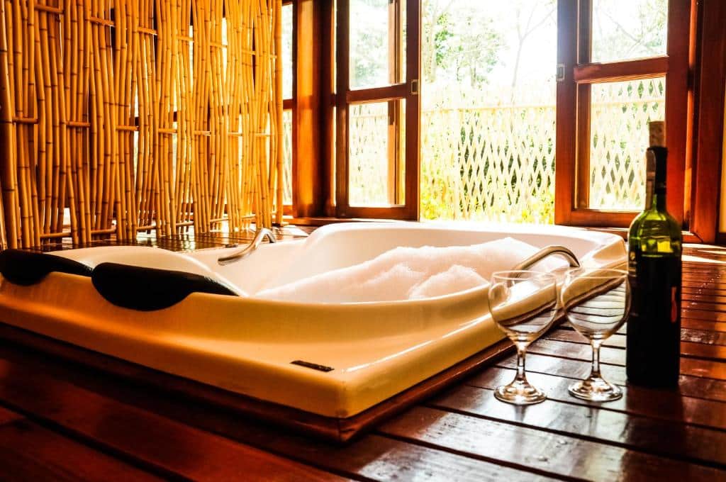 Canto da Floresta Ecoresort com Banheira de hidromasssagem em cabana rústica de bambu com taça de vinho e garrafa de vinho branco no deck de madeira com vista para vegetação